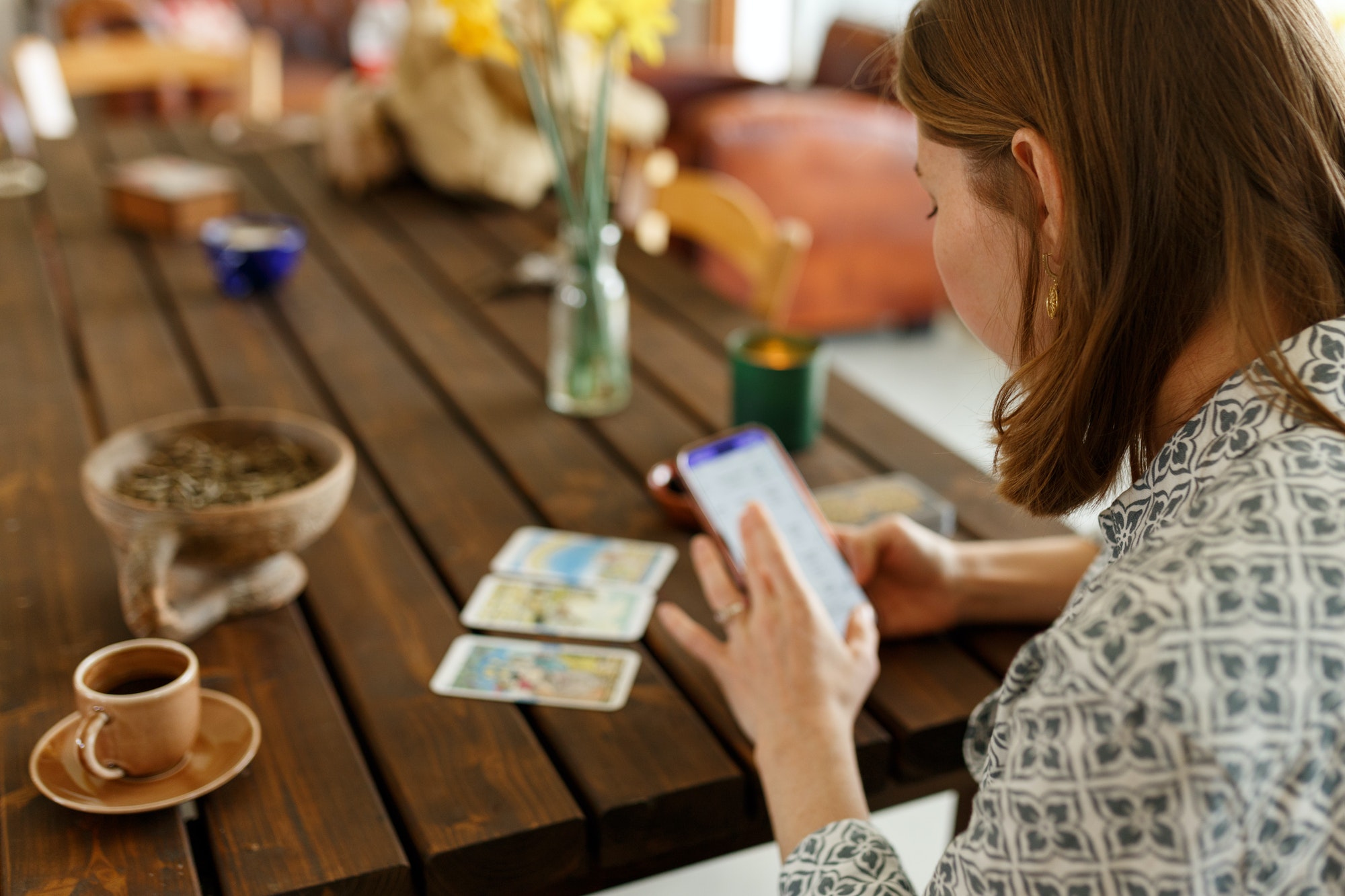 Beautiful young woman is guessing on cards with tarot, runes on wooden table and uses an online